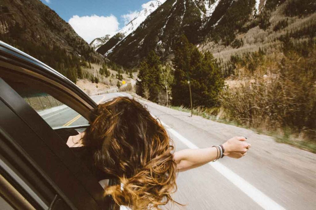Social ethics aren't just rules thrust upon you for no reason. They are there to protect your mind. The five yamas outline the five main social rules you should follow to protect yourself from your own mind. Image of a woman hanging out of the passenger side window of a moving car with her hair whipping in the breeze.