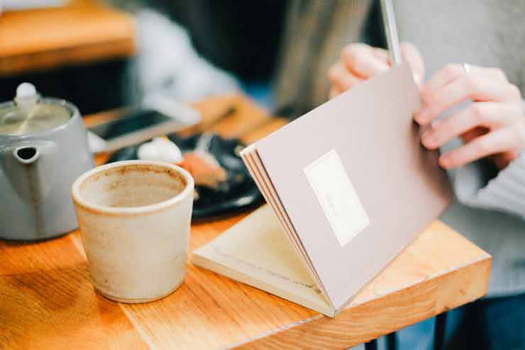 Journaling can not only release day-to-day stress but also help you go deep into your mind and psyche and release other stresses that are bogging you down. Image of somone opening a journal while having a tea.
