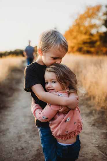 Image of two children a brother and a younger sister hugging each other with wide open plains in the background.