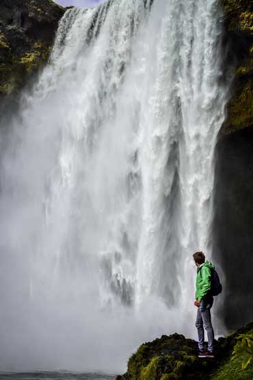 A hiker looking back at a grand waterfall, reminiscent of the neverending flow of life.